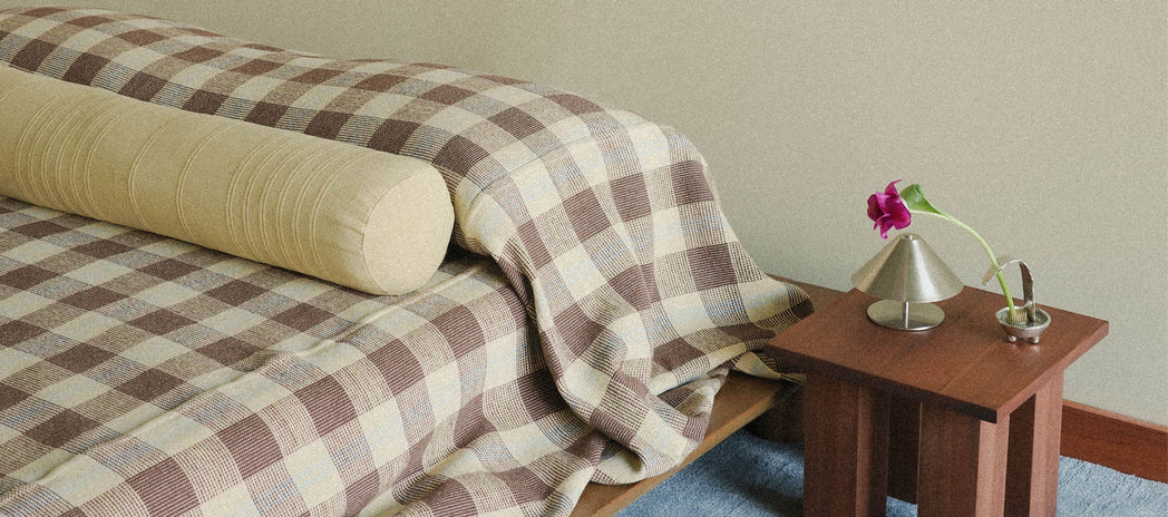 Bed with checkered blanket and wooden side table in a minimalistic room.