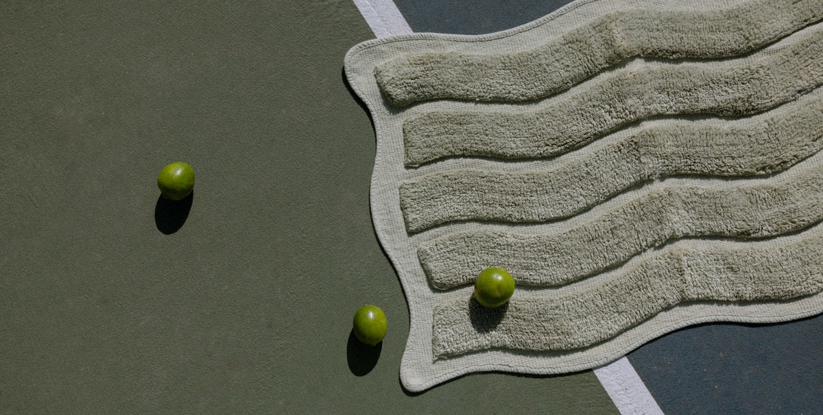 A textured wavy green bath mat, styled on a dark green tennis court with three green limes.
