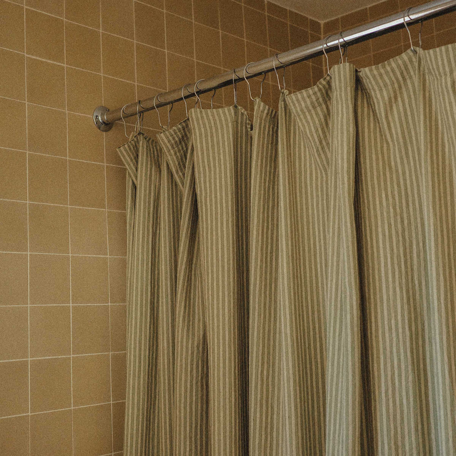 Striped shower curtain hanging on a rod against a tiled bathroom wall.