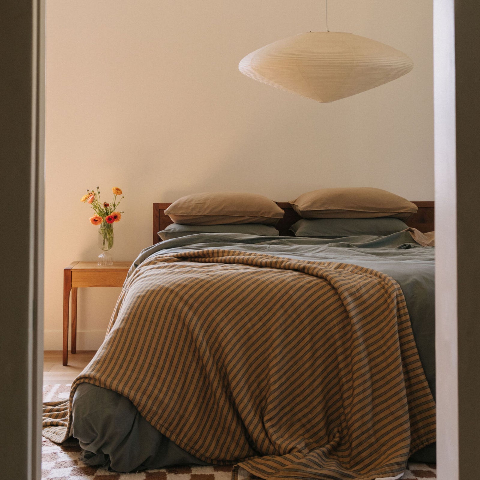 A bedroom setting with a striped coverlet and Dune pillowcase stacked on top of Pacific pillowcases and a Pacific duvet cover