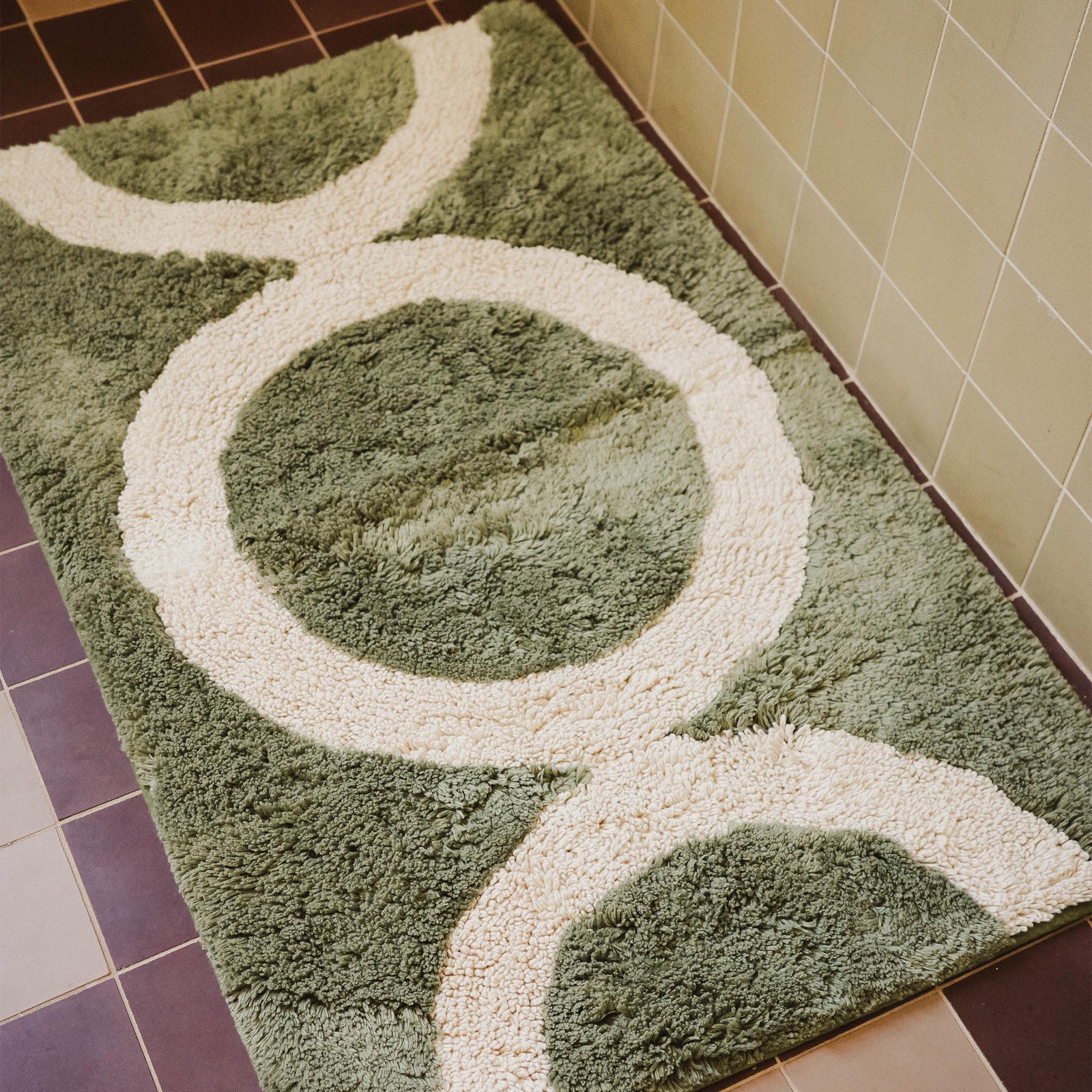 A green tufted bathmat with a beige circle pattern in a bathroom.