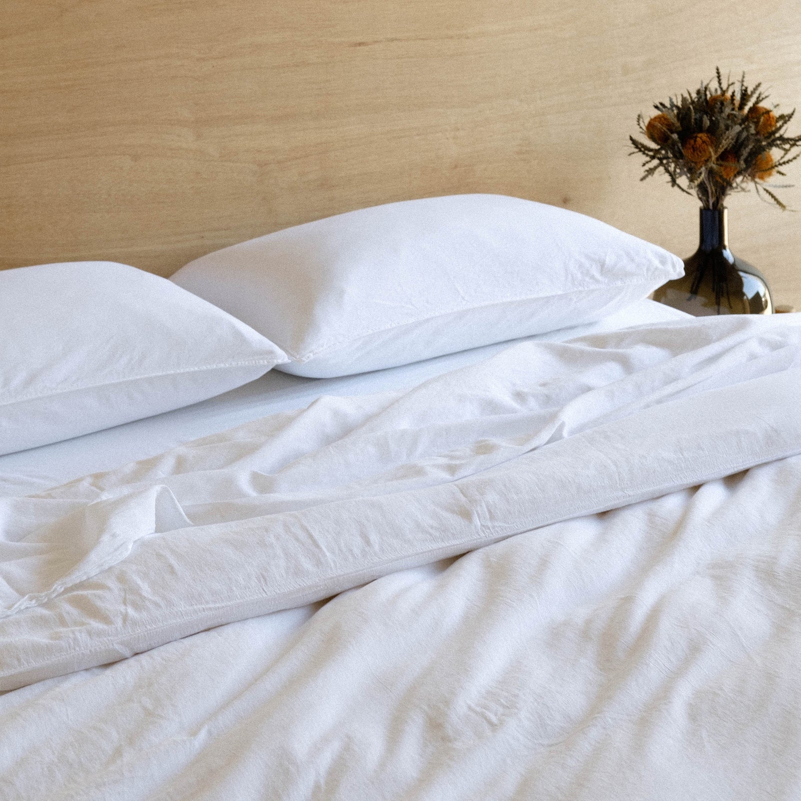 The top half of a bed dressed in white matte sateen sheets against a wooden headboard