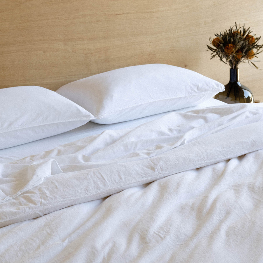 The top half of a bed dressed in white matte sateen sheets against a wooden headboard