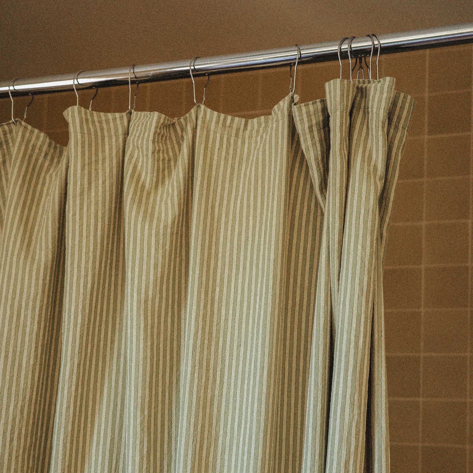 Striped shower curtain hanging on a rod against a brown tiled wall.