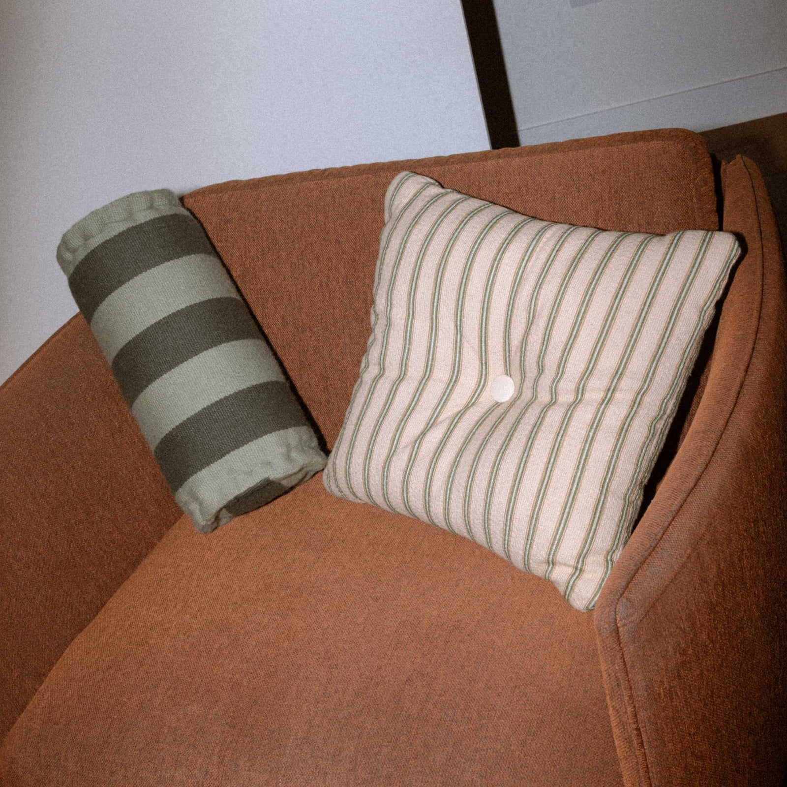 Two green striped pillows on a brown couch against a white wall.