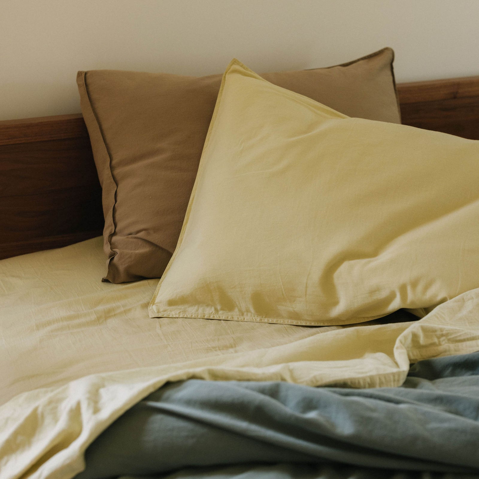 A close up of a bed dressed with Límon sheets and a pillow against a Dune pillow with a green duvet cover in the foreground. 