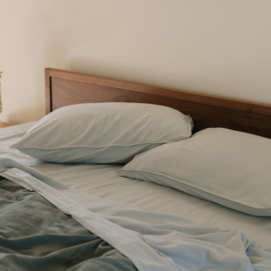 A bed with pale blue / Mist sheets and pillowcases shown with a deeper green duvet cover against a dark brown headboard