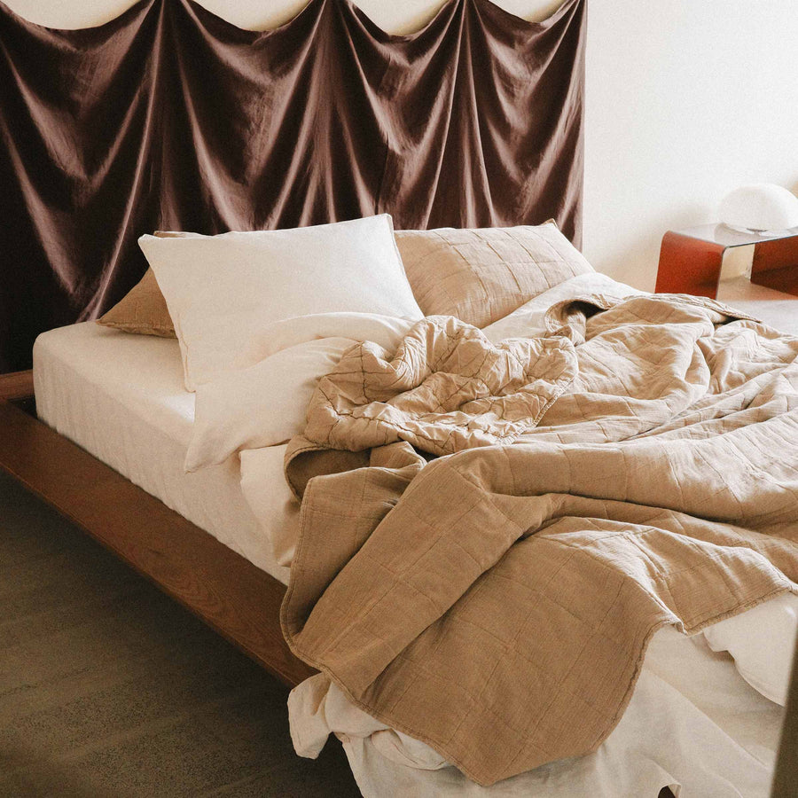 Unmade bed with a brown quilt and cream sheets in a bedroom setting