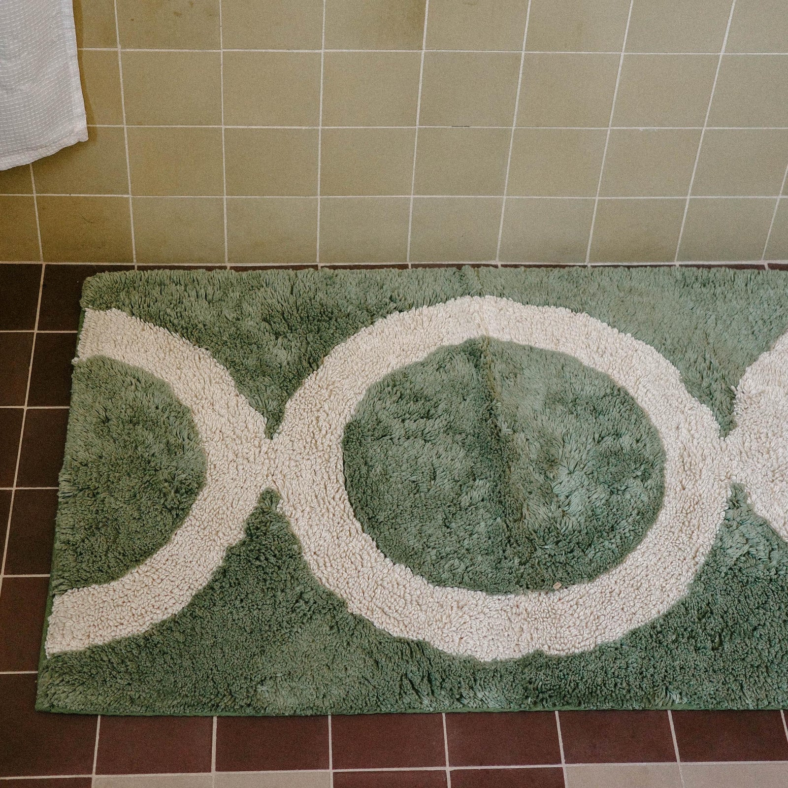 Close up of a green tufted bathmat with a tan circle pattern in a bathroom.