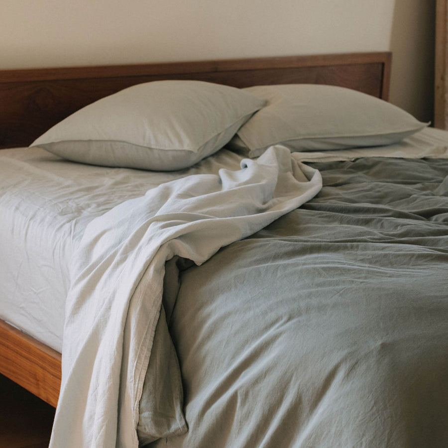 A bed with Mist / pale blue sheets and a matte green duvet cover 