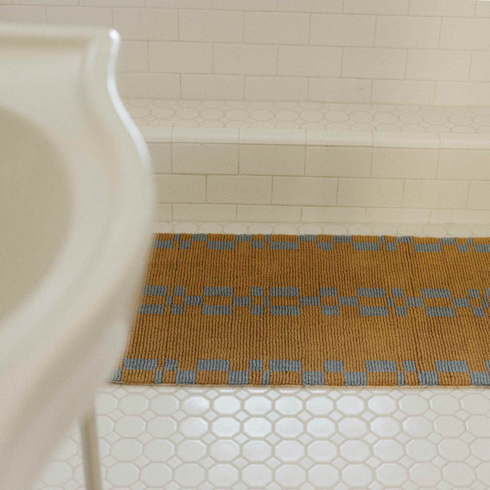 a brown bathmat with a blue geometric pattern on a white tile bathroom floor.