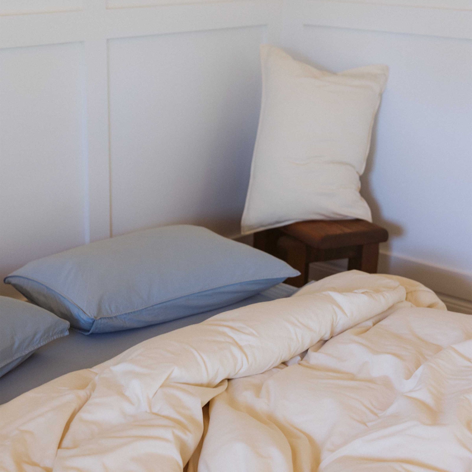 A bedroom scene with Afina / Blue pillows paired with a cream duvet. There is a cream pillow resting on a chair next to the bed