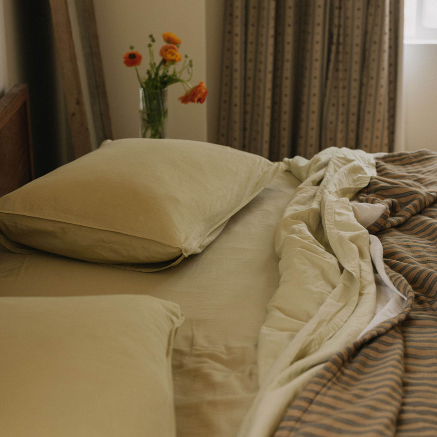 Close up of the top half of a bed with a striped coverlet paired with organic mate sateen Límon sheets and pillows in a bedroom setting