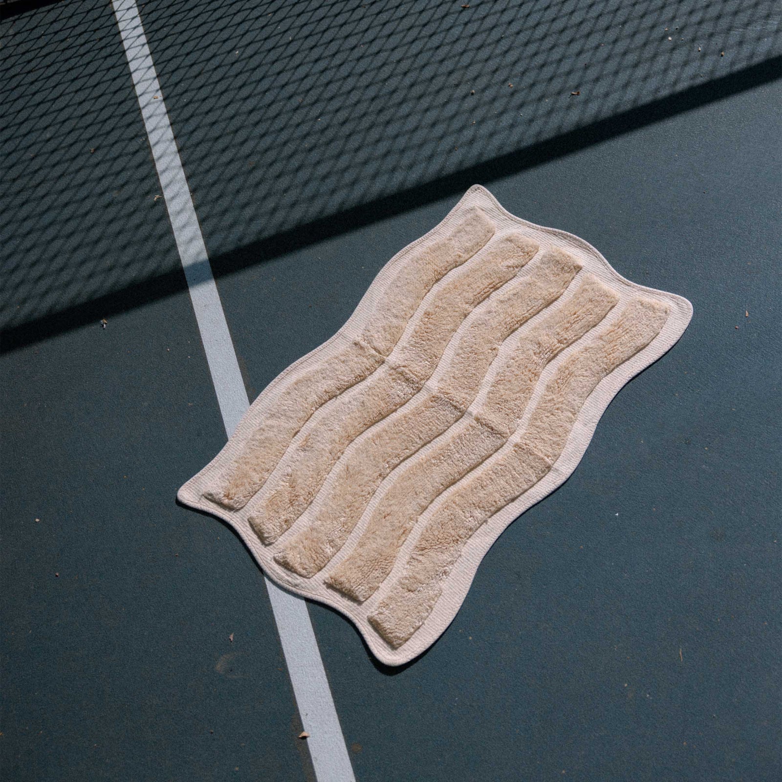 yellow bath mat with wavy pattern on the dark surface of a tennis court.
