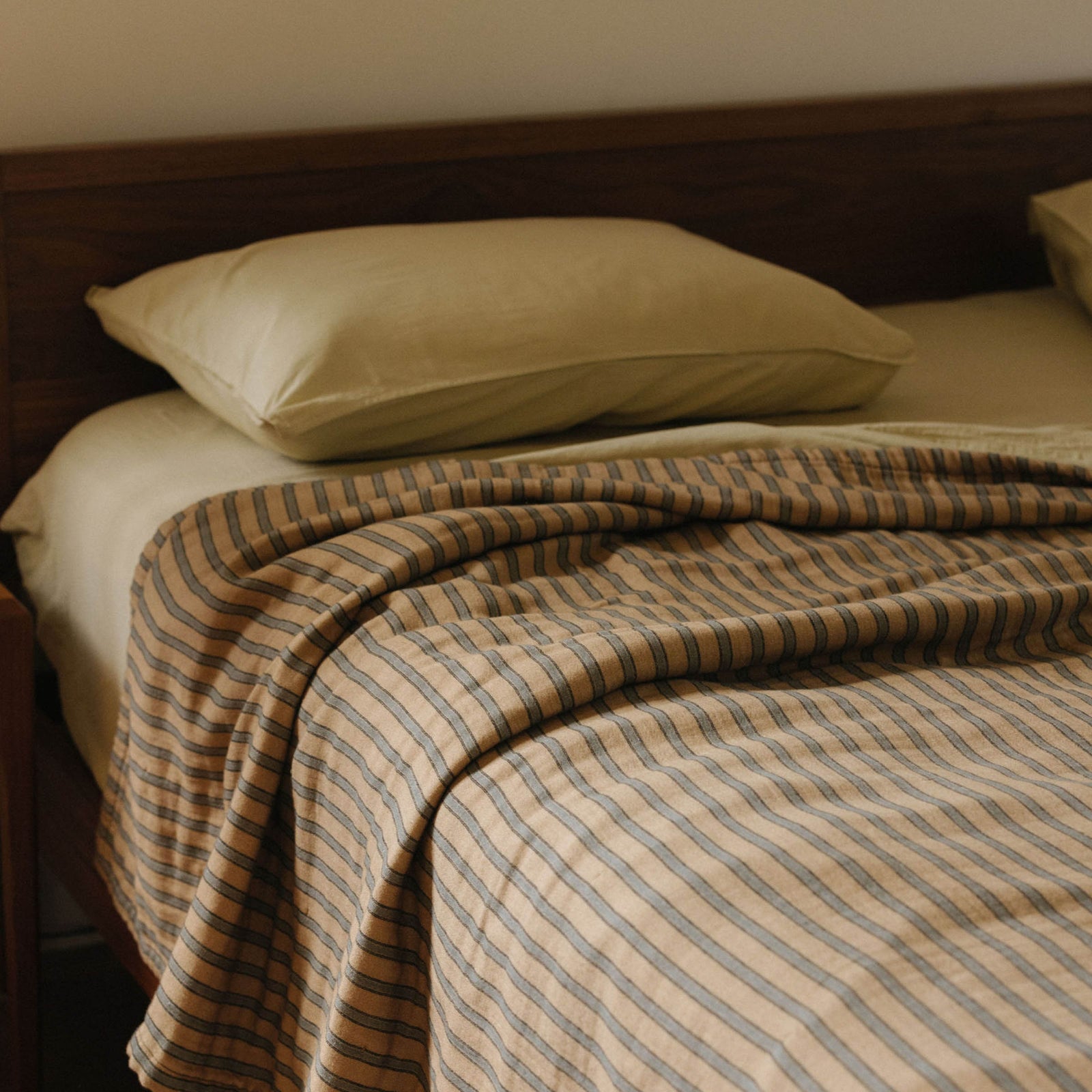 A bed with a striped coverlet over Límon sheets and a Límon pillow against a dark wood headboard