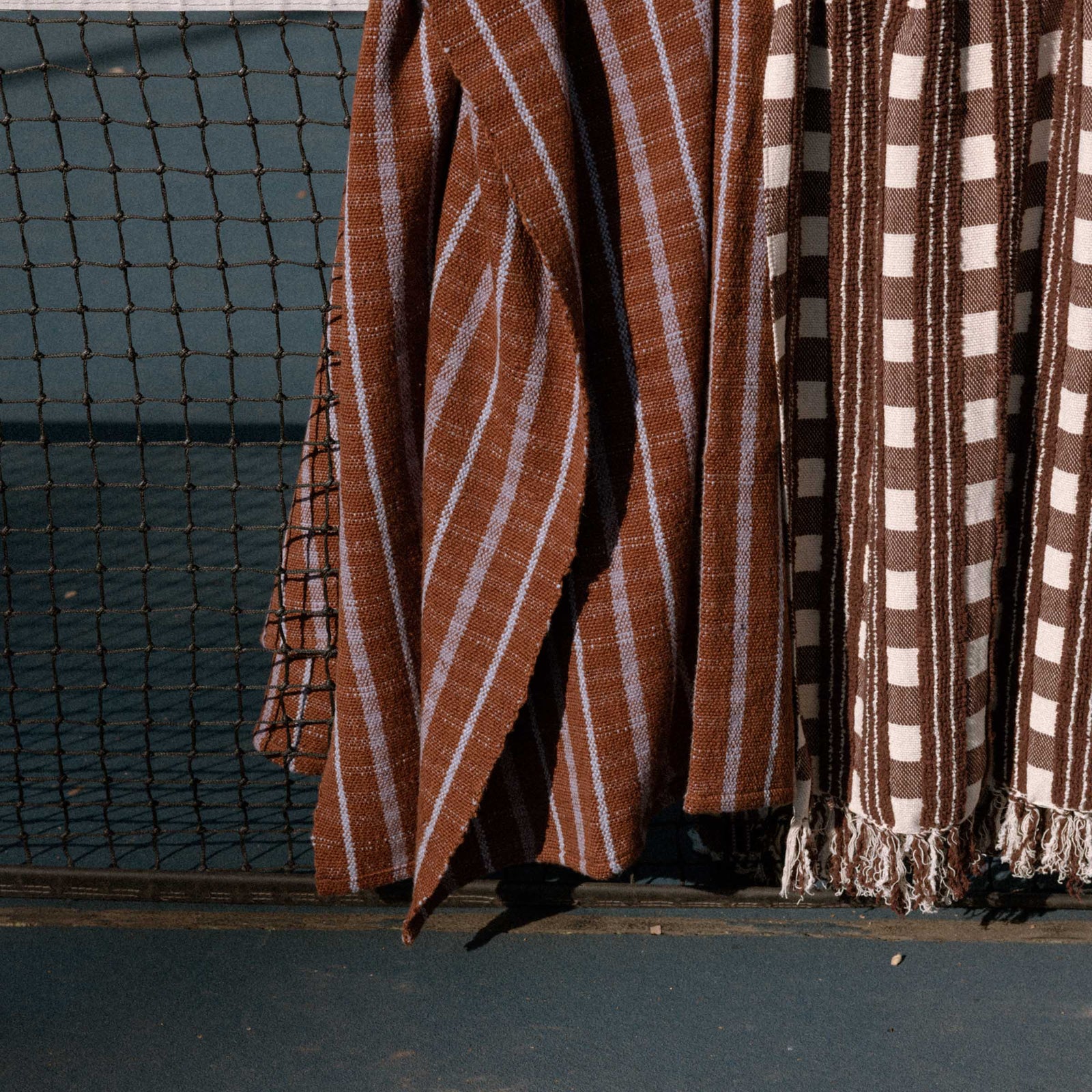 Two different brown patterned blankets draped over a net on a tennis court.