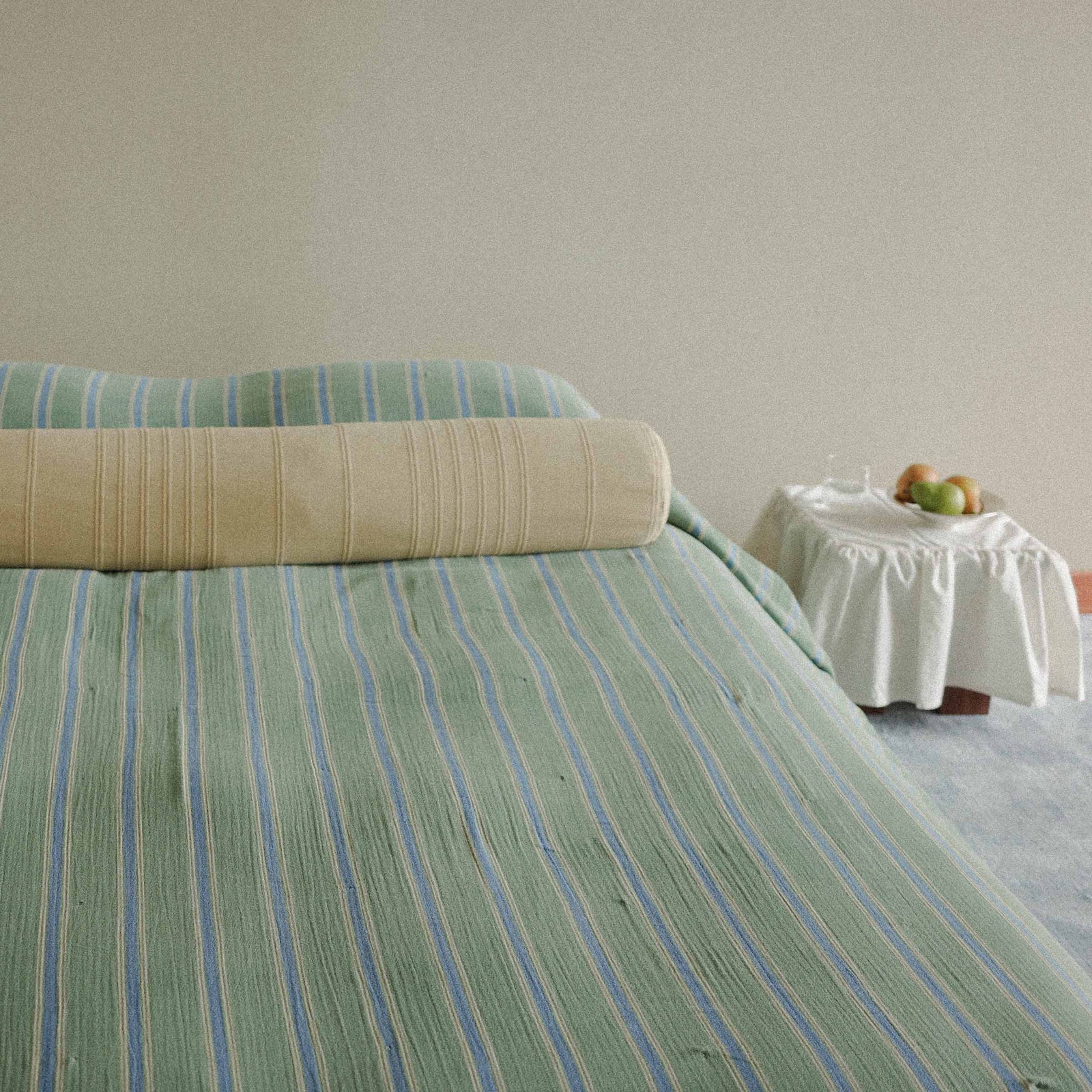 Bed with green striped bedding and a side table with fruit in a room.
