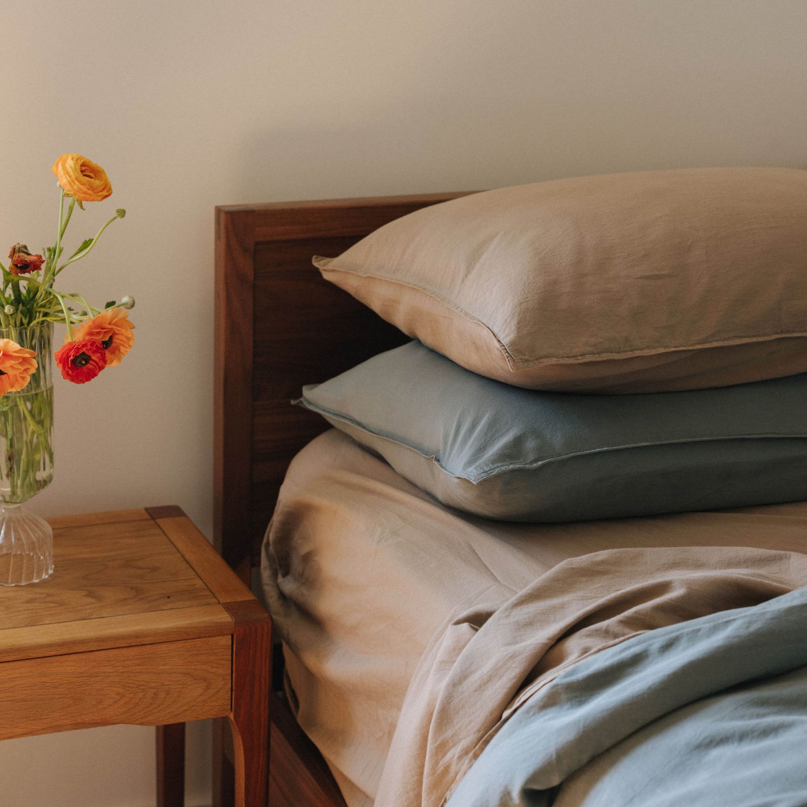 The top half of a bed with Dune and Pacific pillowcases in organic matte sateen on a bed with Dune and Pacific sheets in a bedroom setting