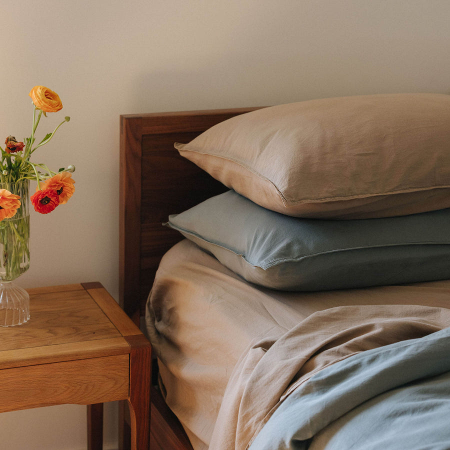 The top half of a bed with Dune and Pacific pillowcases in organic matte sateen on a bed with Dune and Pacific sheets in a bedroom setting