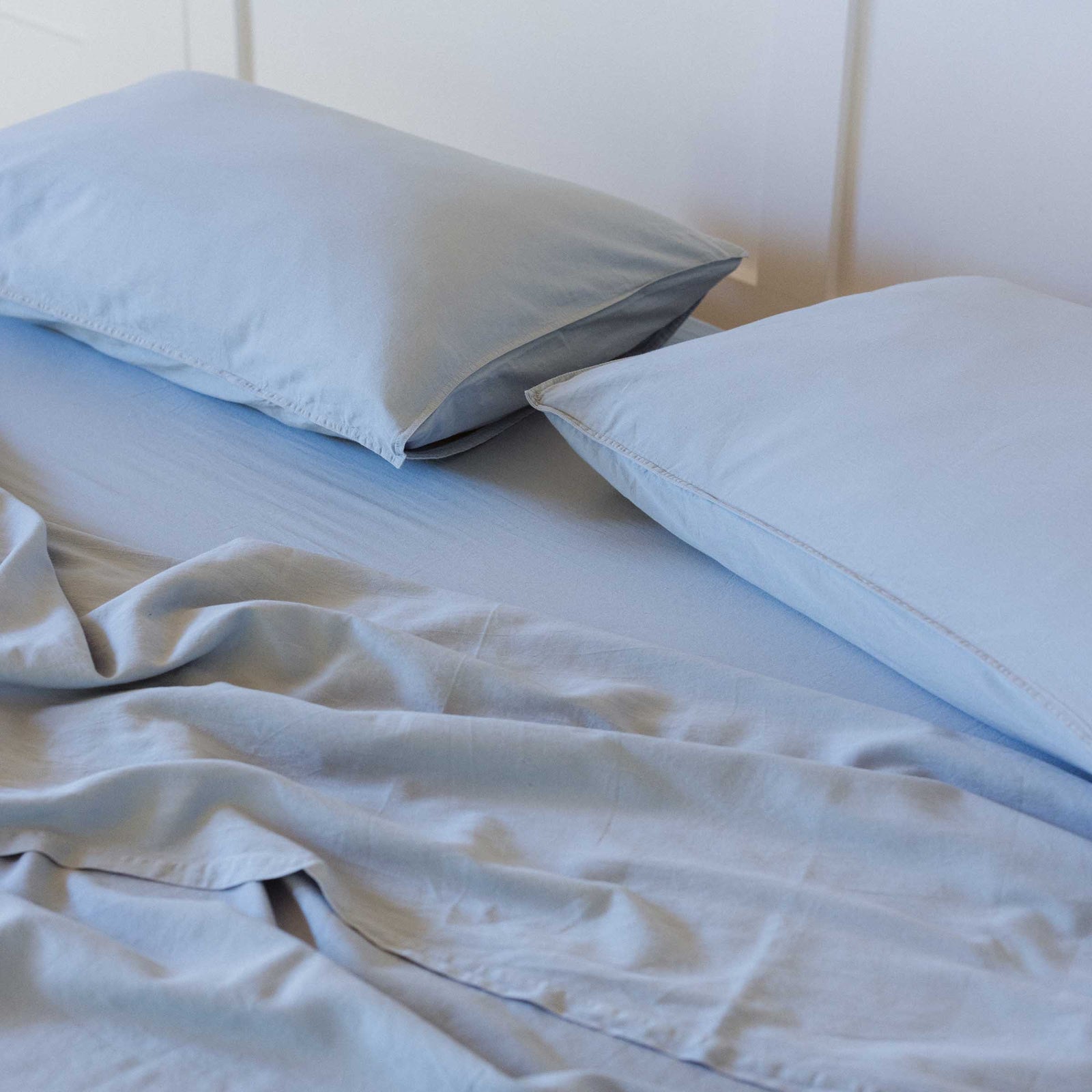 A close up of the top of the bed with two pillows and sheets in blue / Afina