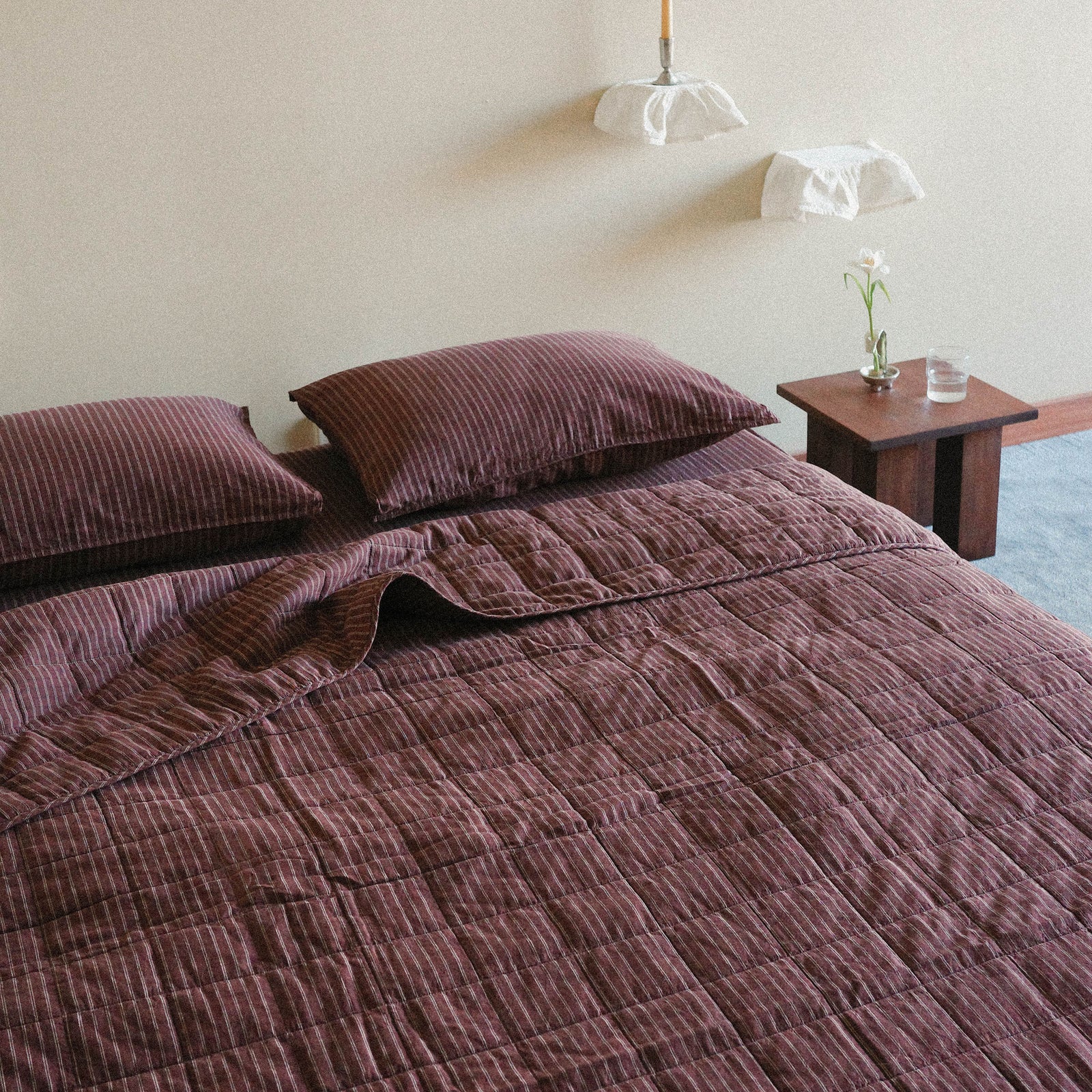Brown striped quilt / bed cover on a bed with matching pillows in a bright bedroom setting.