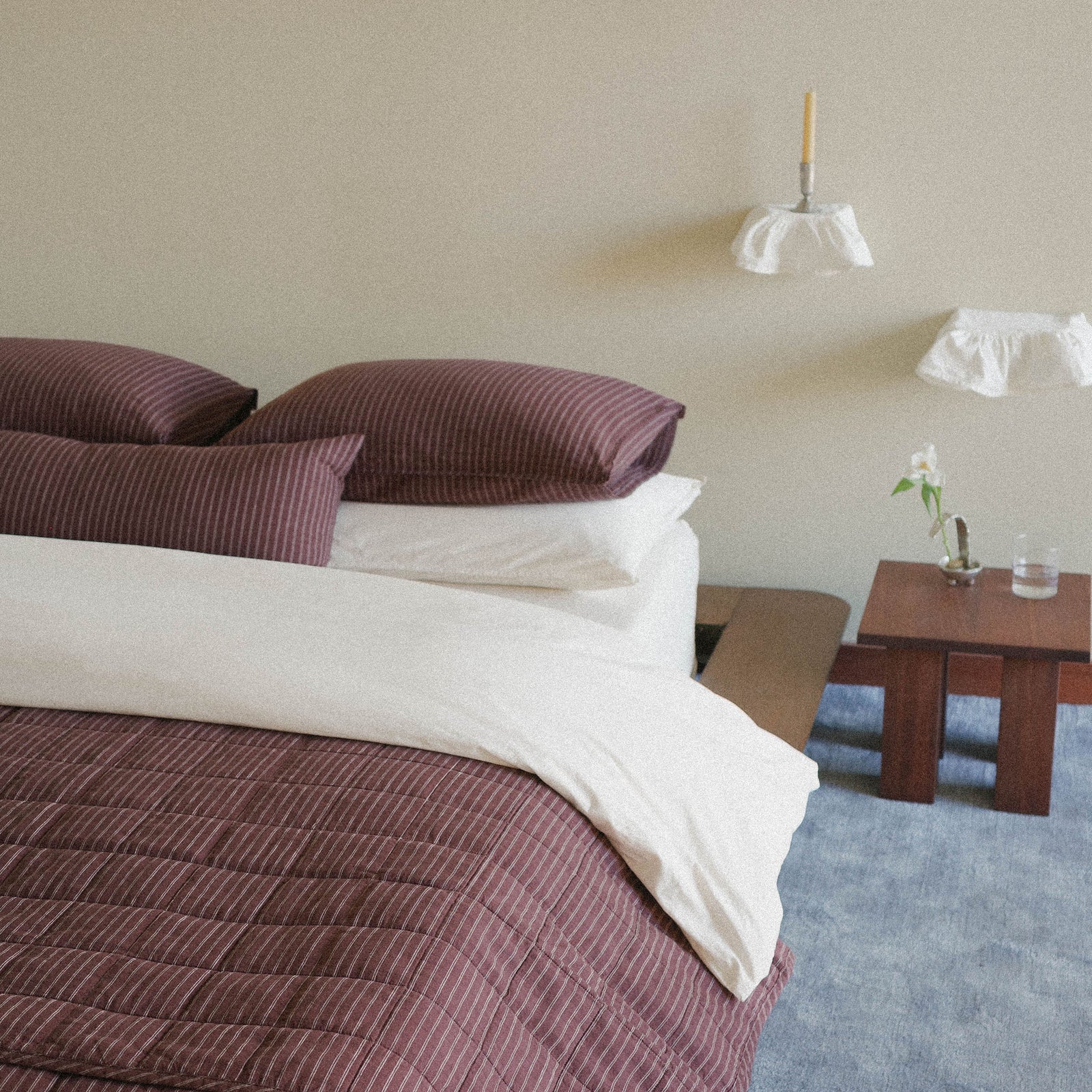 Bedroom with a bed featuring brown striped and white bedding, a nightstand with a glass and blooming flower, delicate fabric shelving 