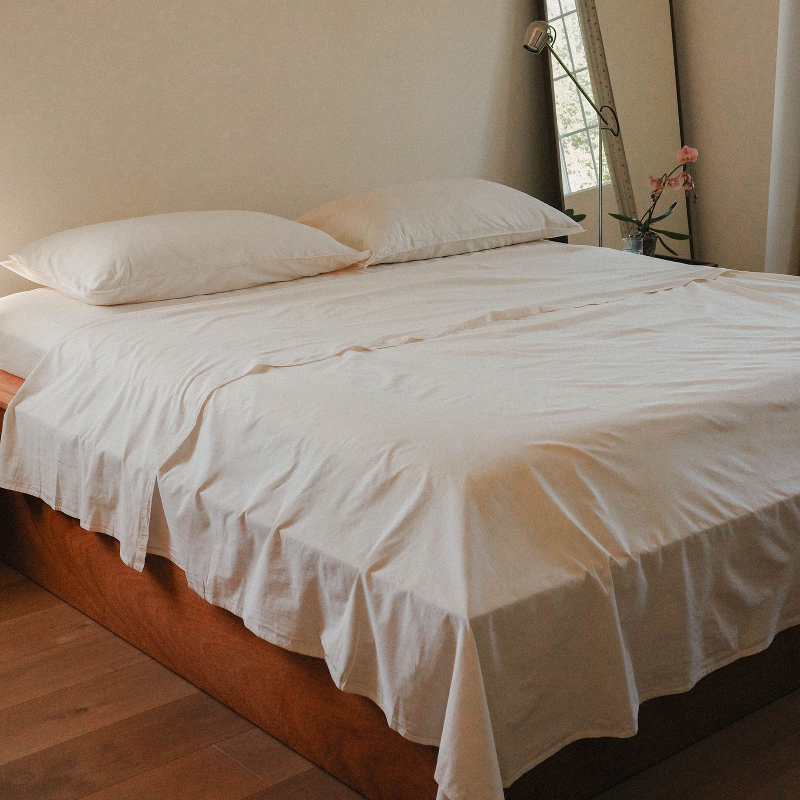 Bed with cream bedding in a room with a mirror and curtains.