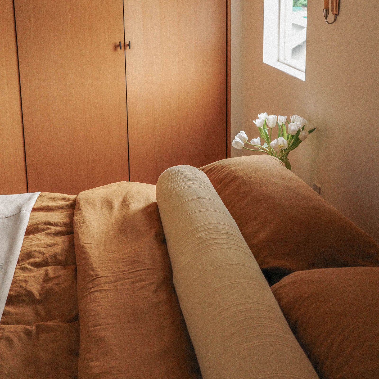 Morrow Soft Goods Hemp Cotton Duvet Cover in Willow, Marta Coverlet in White and Devi Bolster in Maiz. Bedroom Lifestyle Image Crop with Wood Closet Behind