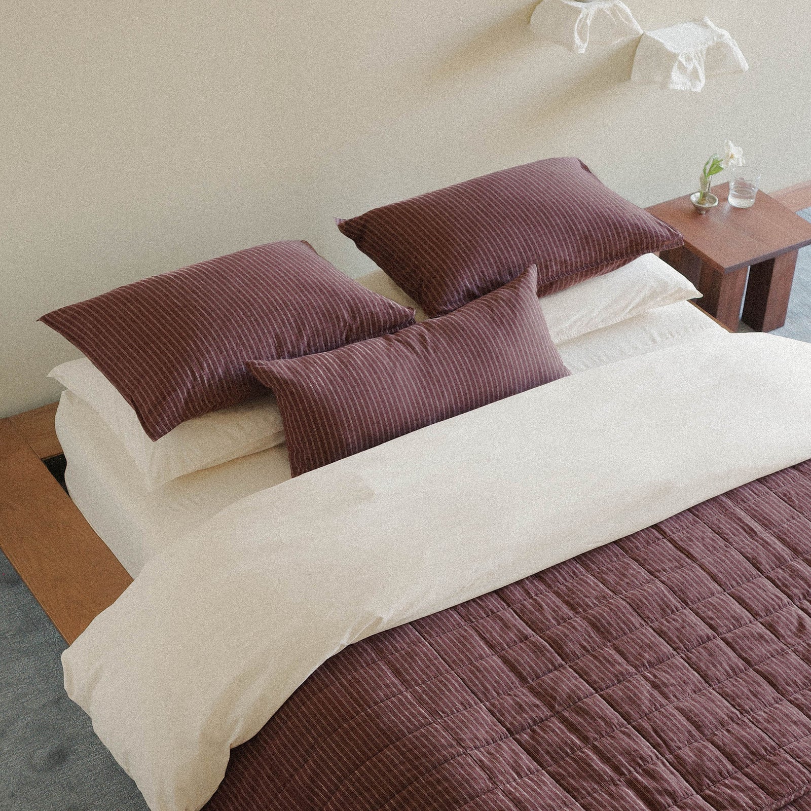 Neatly made bed with brown striped bedding including a lumbar pillow, quilt and cream / white bedding on a wooden bed frame