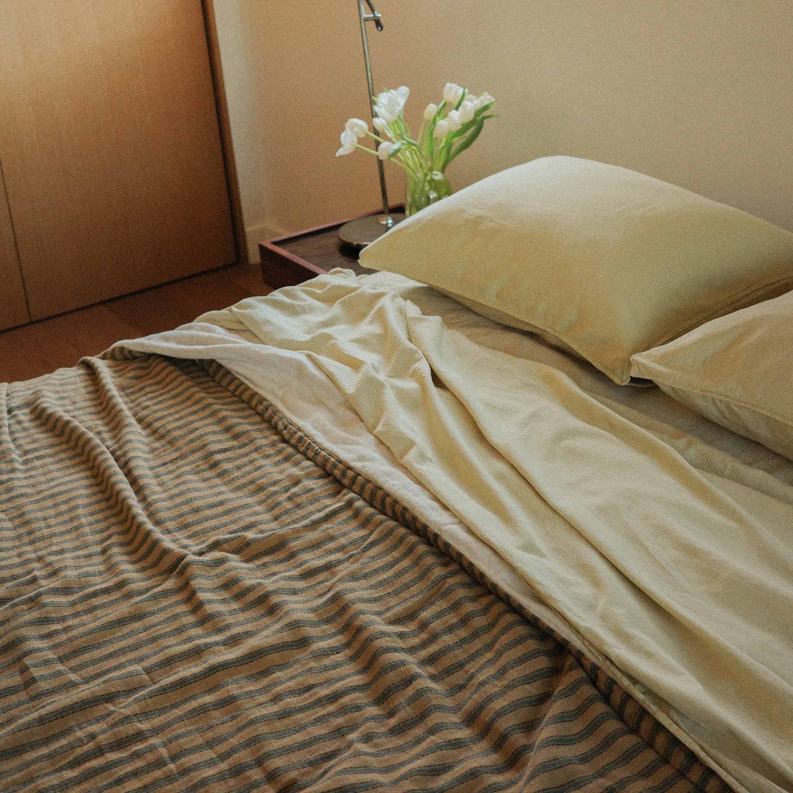Bed with striped coverlet and yellow  pillows and sheets in a bedroom setting