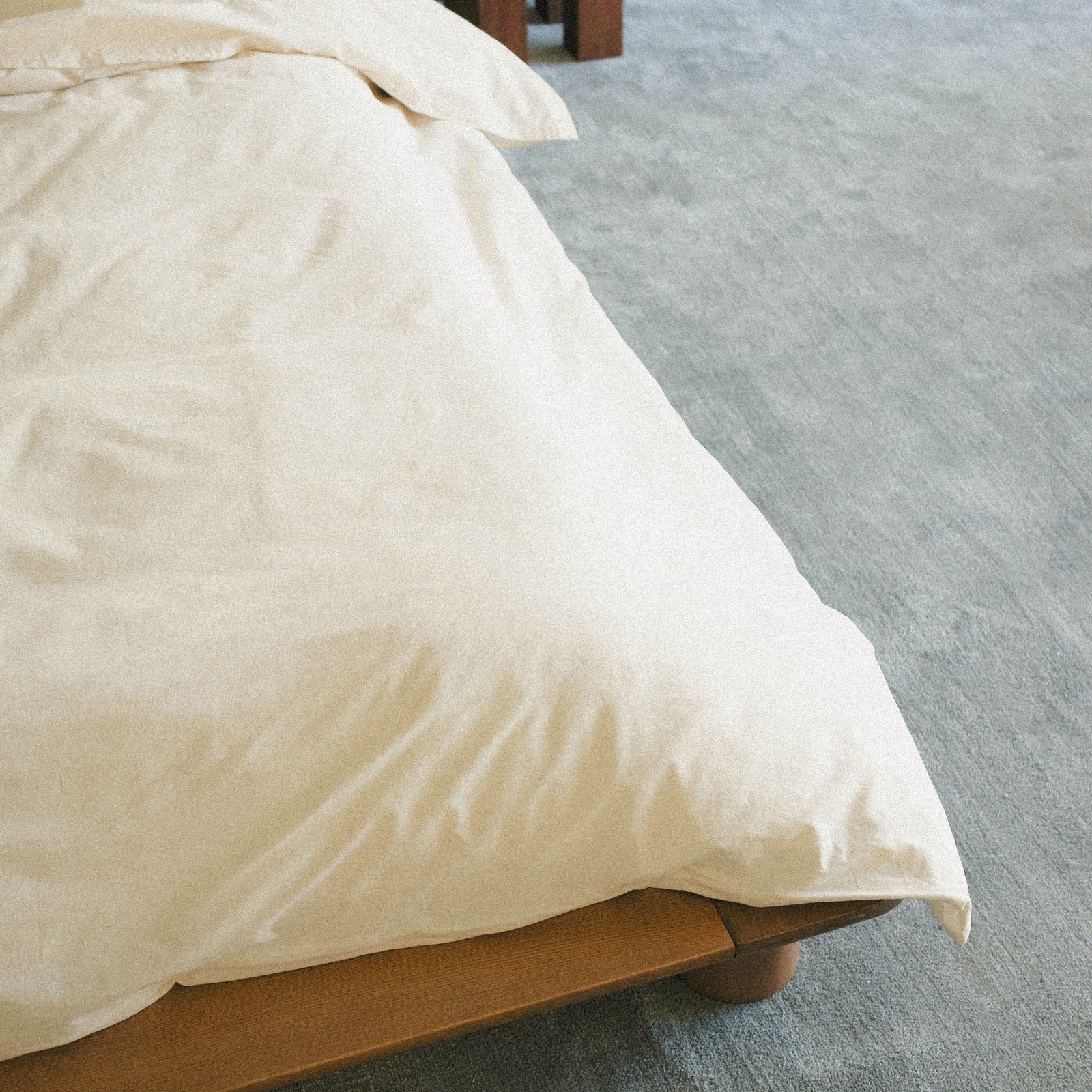 Close-up of a cream duvet cover on a bed with a blue carpeted floor.