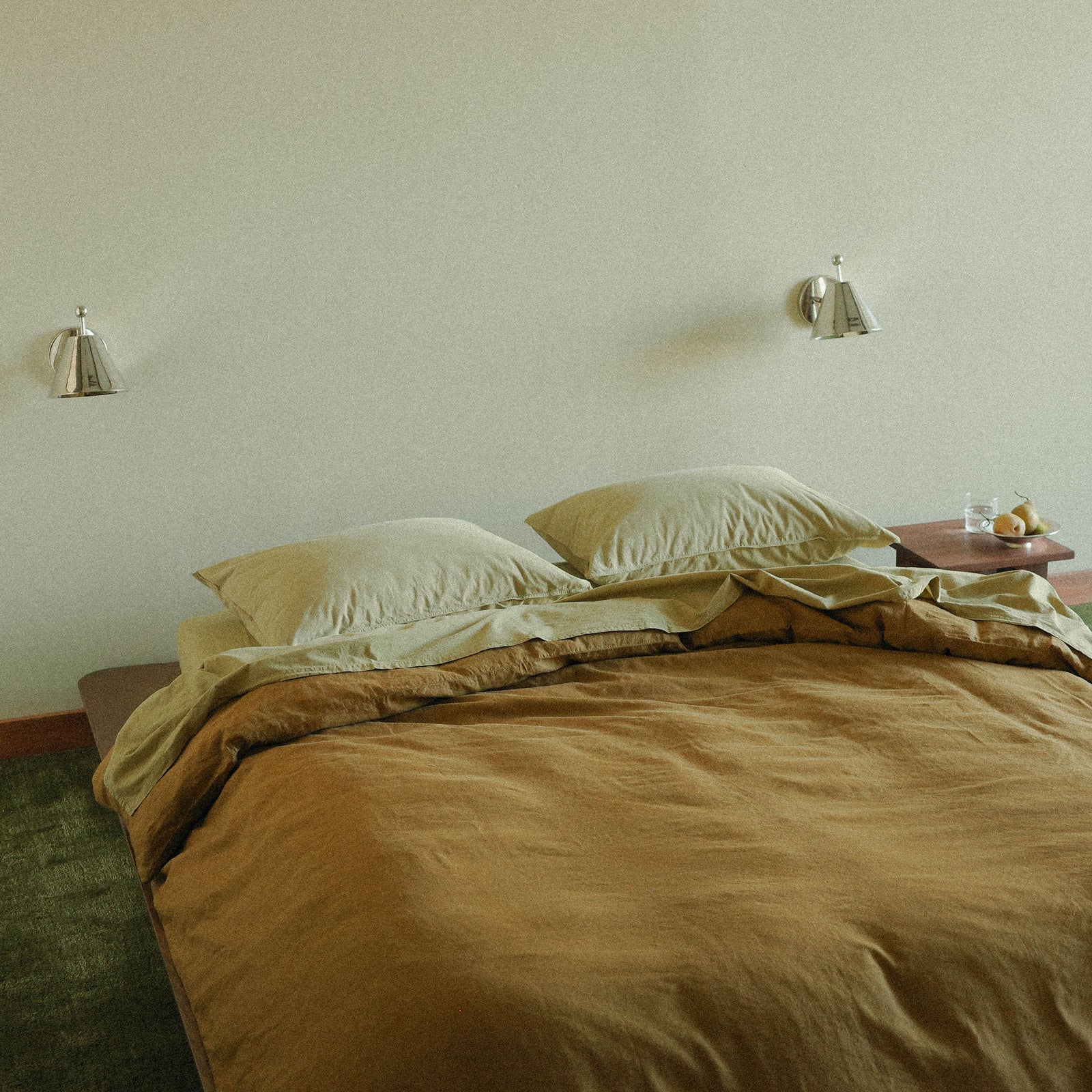 Bedroom with a bed and nightstands against a plain wall with two chrome wall sconces.