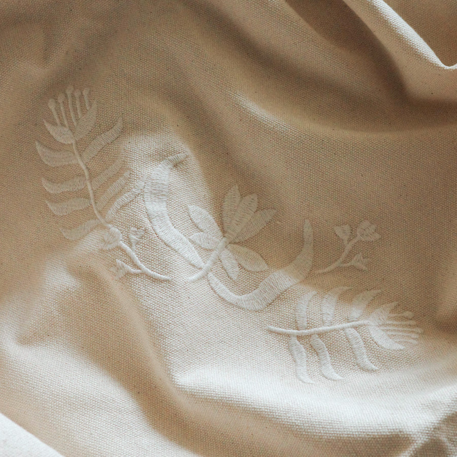 Close-up of a beige fabric surface with white embroidered botanical and leaf motifs.
