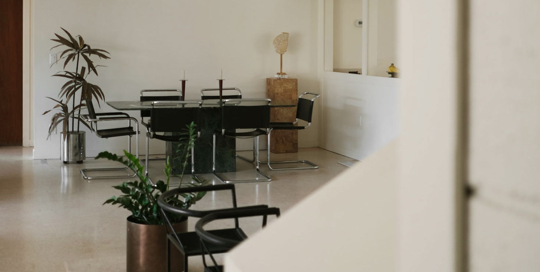 Mid century modern dining room with a glass table, black chairs and tall i ndoor plants