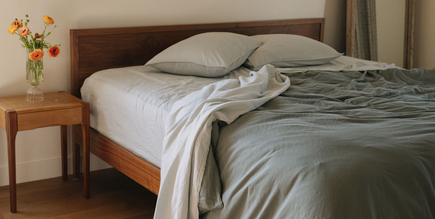 Bedroom with a wooden bed frame, light blue and green bedding, and a small table with flowers.