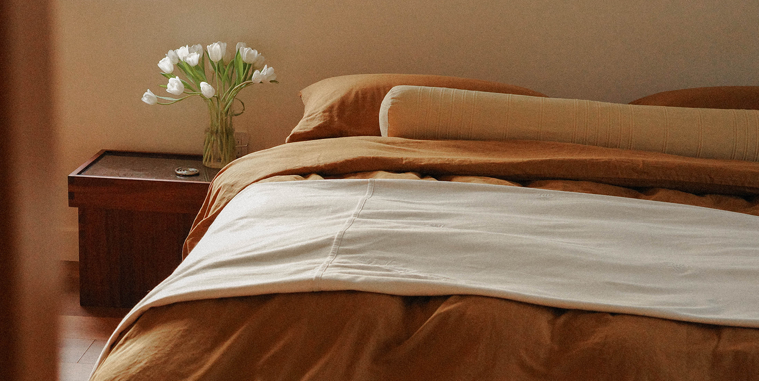 Bed with brown bedding and white flowers on a wooden nightstand.