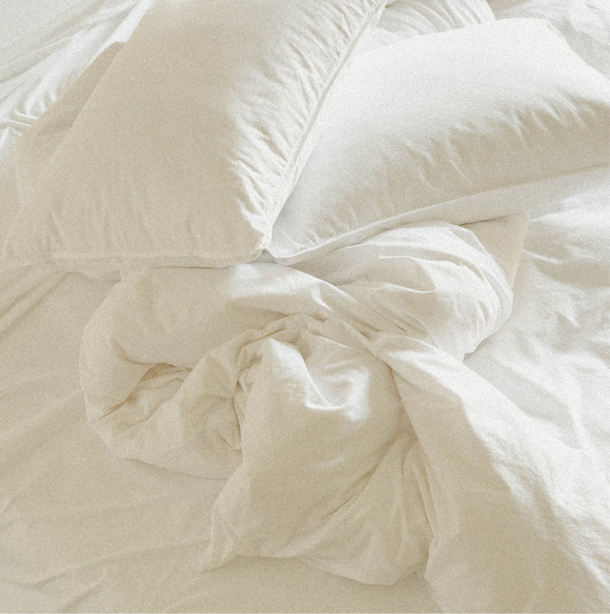 White cotton bedding set with two pillows and rumpled duvet on a bed.