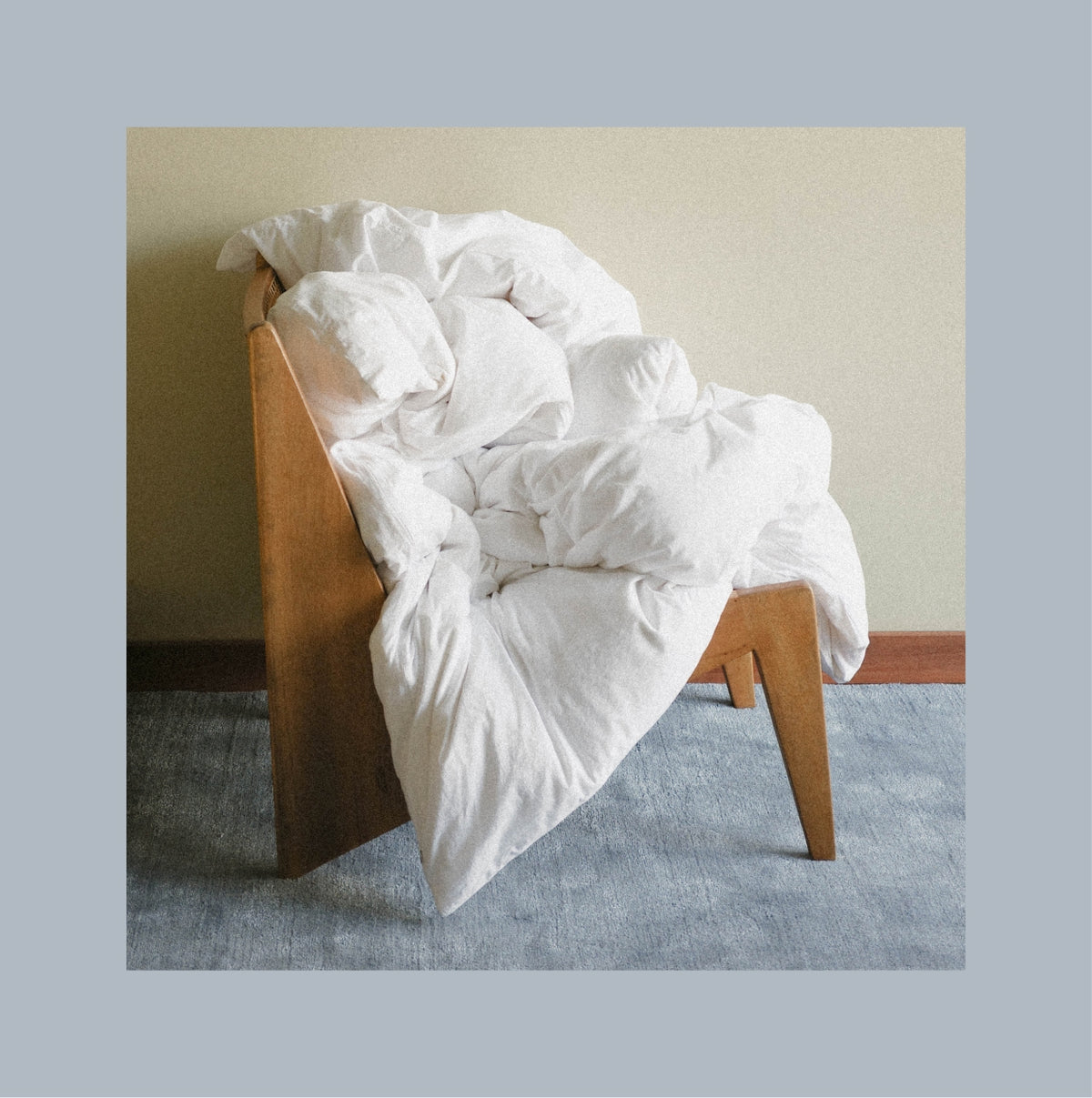 A white duvet thrown on a wooden chair in a room with a blue rug.