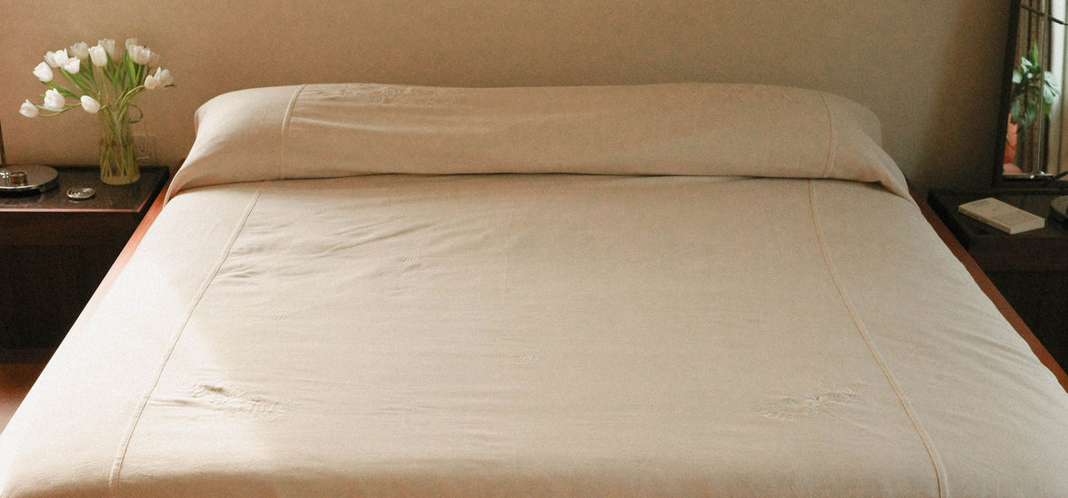 A bed dressed in a white coverlet positioned in a warmly lit bedroom.