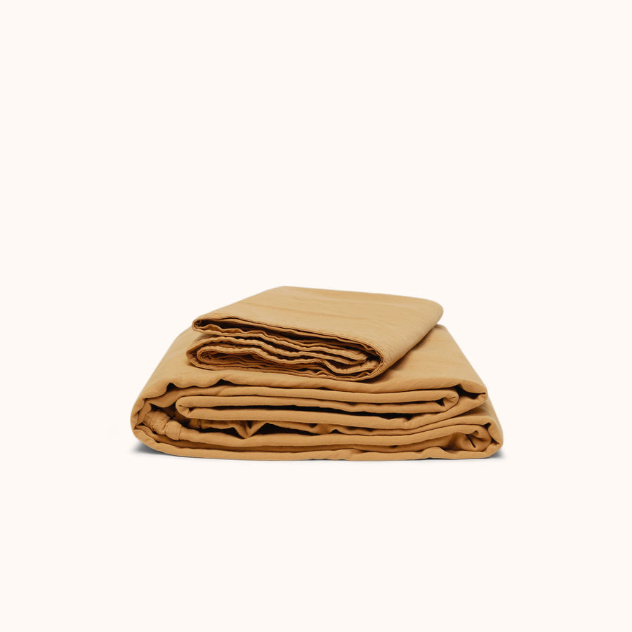 Folded light camel colored sateen sheet set on a white background