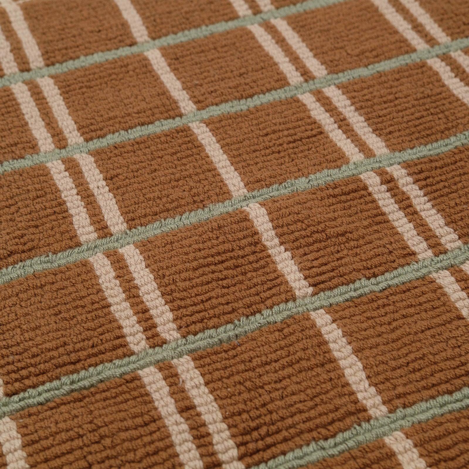 Close up of a brown mat with intersecting green and tan stripes showcasing the loop construction.
