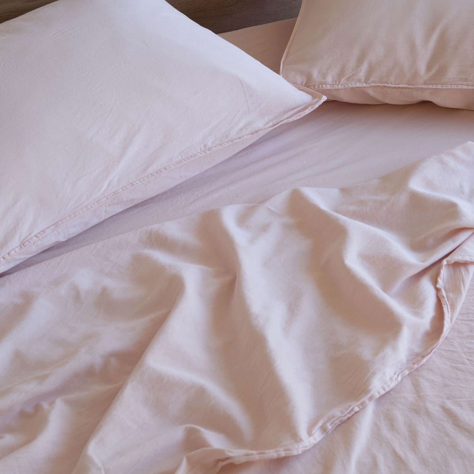 A close up of a bed with light pink sheets and pillows