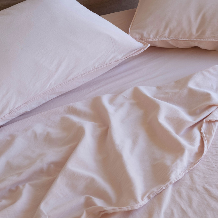 A close up of a bed with light pink sheets and pillows