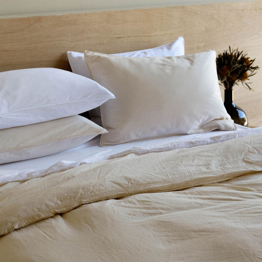 A bed dressed with various shades of cream and beige sheets and pillows 