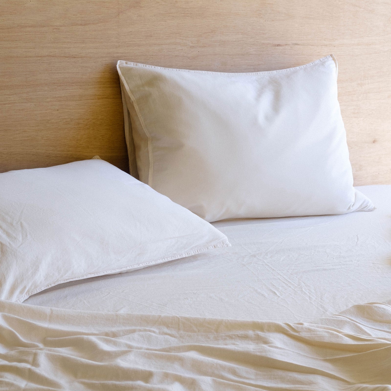 A close up of two oat matte sateen pillow on a bed of oat matte sateen sheets in a bright room