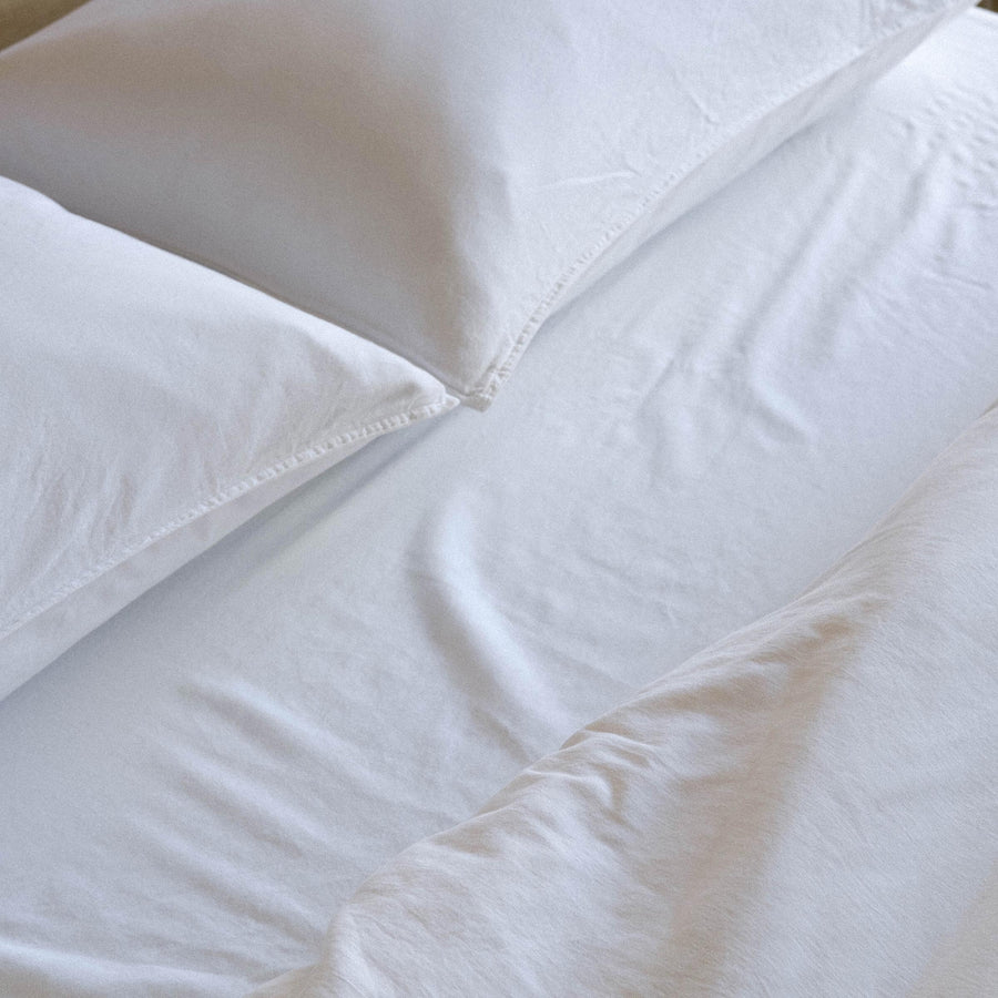 Close up on two pillows and a bed made with white matte sateen sheets